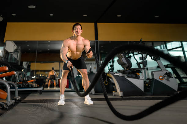 joven asiático hace ejercicio con cuerdas de batalla en un gimnasio de fitness saludable. hombre asiático con cuerda de batalla cuerdas de batalla ejercicio en el gimnasio de fitness. - body care asian ethnicity body building toughness fotografías e imágenes de stock