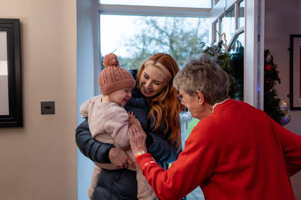 There's My Gorgeous Great Granddaughter A medium shot of a senior woman opening her front door to her granddaughter and her great granddaughter at Christmas. She welcoming them as they walk through the door. grandmother child baby mother stock pictures, royalty-free photos & images