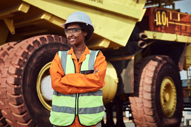 Woman Mine Worker A young African woman mine worker is standing in front of a large haul dump truck wearing her personal protective wear miner stock pictures, royalty-free photos & images