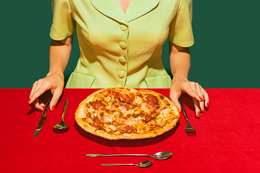 Food pop art photography. Delicious, fresh baked italian pizza with ham and sausage on red tablecloth isolated on green background. Vintage, retro style. Complementary colors, Copy space for ad, text