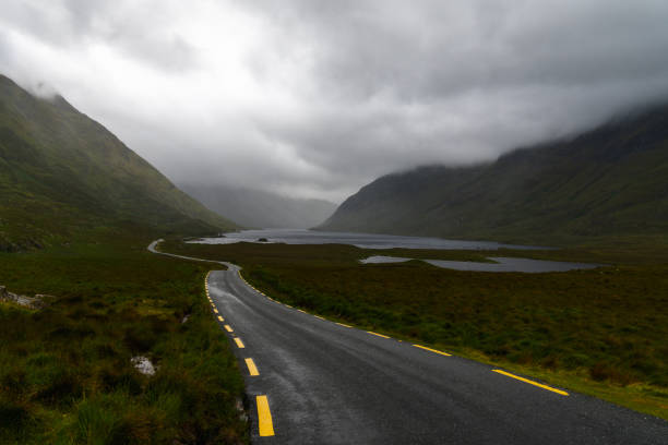 stretta autostrada dalla cima nera conduce attraverso una valle di montagna coperta con nebbia e nebbia e laghi sul fondovalle - republic of ireland mayo road lake foto e immagini stock