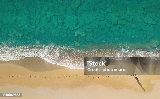 istock Woman walks on the beach along breaking waves leaving footprints on a sand, aerial view directly above 1410869538