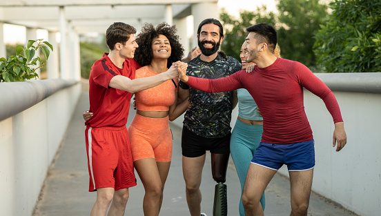 Sporty multiracial friends celebrate their workout outdoors while shaking hands with each other