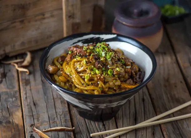 Photo of Beef udon served in a bowl isolated on wooden background side view of japanese food