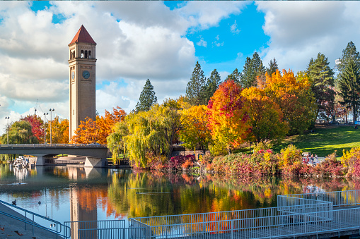 Vivid fall colors of red, orange, and yellow at the Spokane Washington Riverfront Park along the Spokane River with the Great Northern Clock Tower in view.