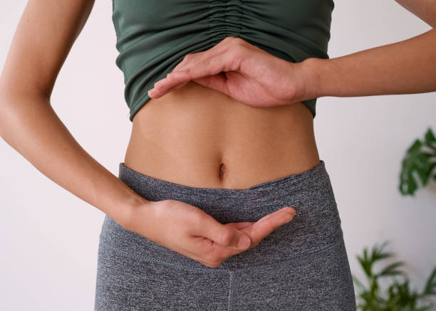close up of a young multi-ethnic woman's stomach cupped by her hands - multi vitamine stockfoto's en -beelden