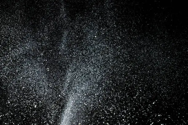 Texture of scattered flour in the air, dark background.