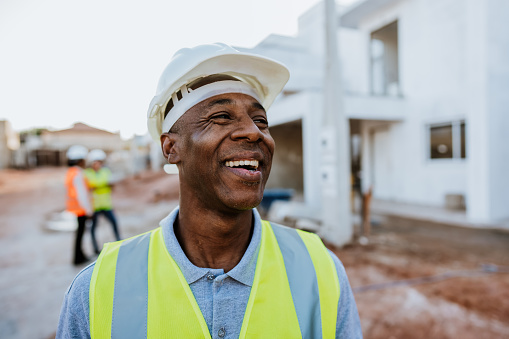 Happy man, construction and face with arms crossed for engineering, project management and labor. Portrait, smile and male builder at building site for property development or infrastructure