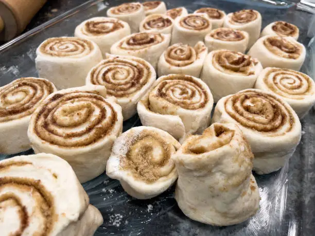A baking tray full of uncooked cinnamon rolls. Spirals of cinnamon and buttery brown sugar filled dough.