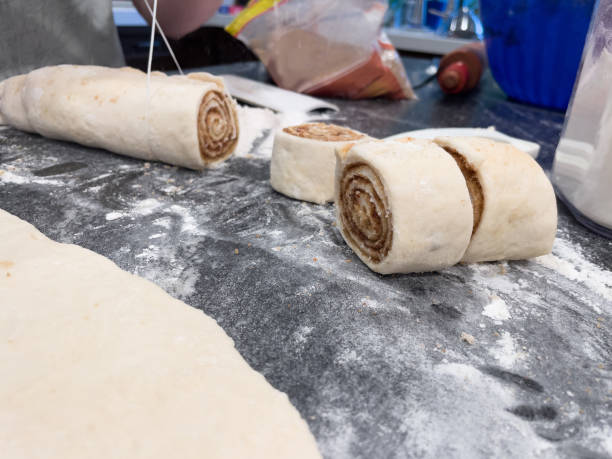 unbaked dough rolled up with cinnamon, butter and brown sugar. Cutting rounds of dough with floss for making cinnamon rolls stock photo