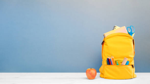 istock Backpack with different colorful stationery and apple on table and blue background. Banner design back to school concept background. 1410886831