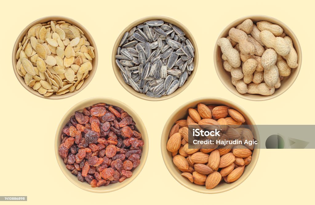 Five types of snacks in brown bowl: sunflower seeds, pumpkin seeds, peanuts, raisins, almonds. Above shot. Different samples Above Stock Photo