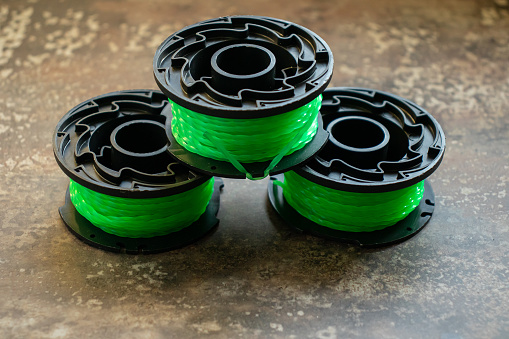 Side view of three replacement green trimmer lines and black plastic spools