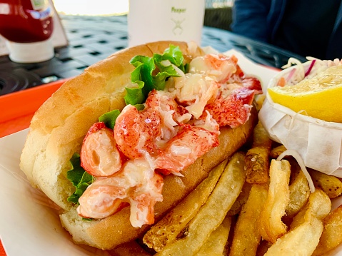 A fresh Maine lobster roll, stuffed with big chunks of claw meat, pictured with sides of fries and other garnishes.