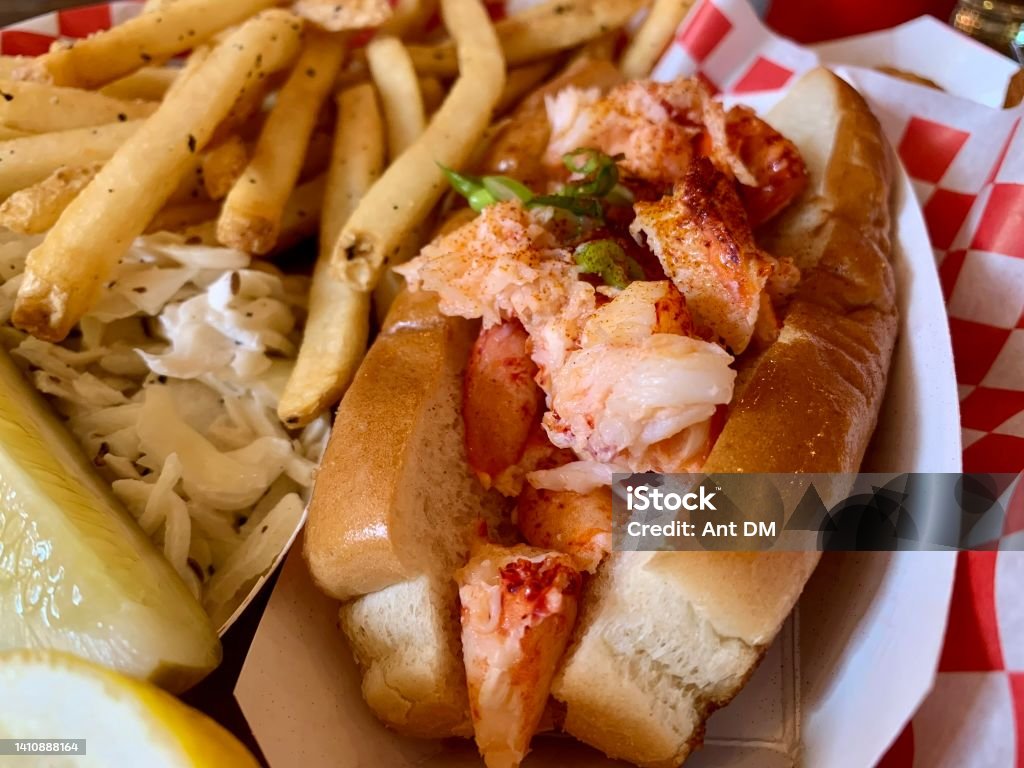 Fresh Maine Lobster Roll A fresh Maine lobster roll, stuffed with big chunks of claw meat, pictured with sides of fries and other garnishes. American Culture Stock Photo