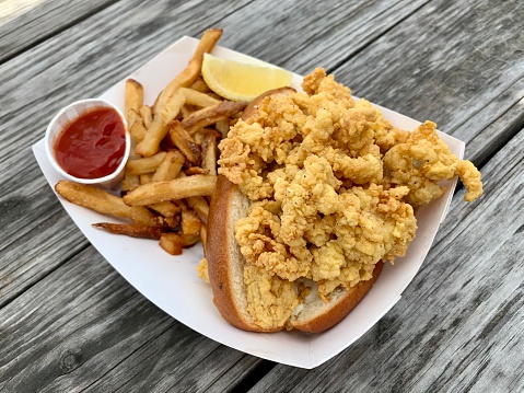 A delicious crispy, fried clam sandwich (pictured with selective focus), served next to French fries and ketchup at a local seafood restaurant.