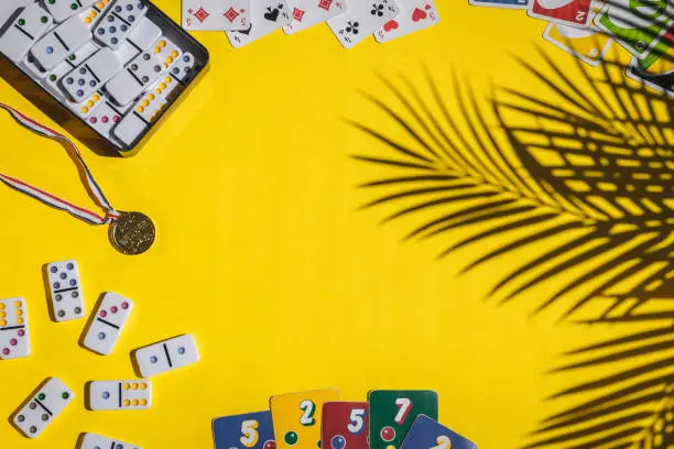 Photo of White dominoes, playing cards, uno, ligretto and winner medal on yellow background. Board game.