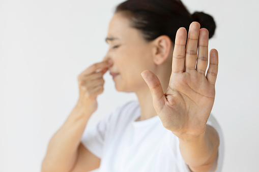 Caucasian female holding nose and showing stop gesture. Representing bad smell.