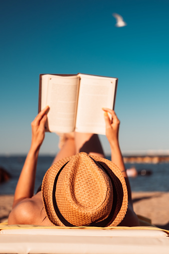 Woman holding a book in the air, reading on the beach.
