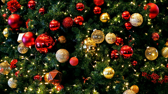 Background of fluffy branches green color New Year trees decorated with beautiful golden shiny sphere balls, toys and ornates against bokehs of Christmas Tree lights