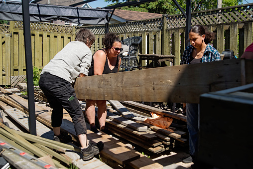 Women constructing a terrace in backyard. There is a body positive mature woman, her teenage latina daughter and her senior friend. Horizontal full length outdoors shot with copy space.