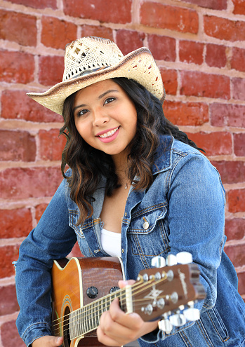 Cowgirl against a brick wall with guitar. Shot in Midway City, California.