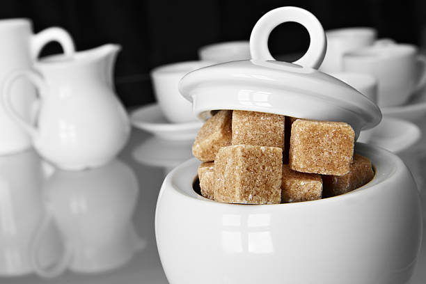 White sugarbowl with brown sugarcubes and some pottery on mixed black and white background