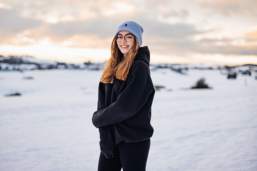 Happy smiling teenage girl standing in front of snow covered winter landscape of Black Forest in Germany, looking over to the camera with a bright smile. Millennial Generation Real People Winter Outdoor Portrait Germany.