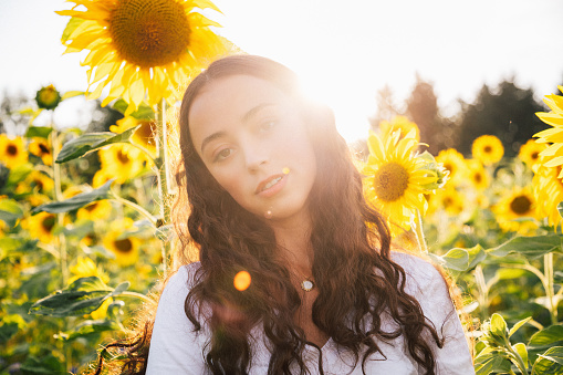 Summertime Feeling. Attractive young teenage woman standing inside sunflower field surrounded with blooming sunflowers backlit from sunset light. Millennial Generation Real People Outdoor Summer Portrait.