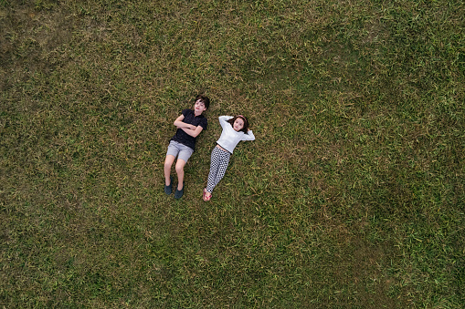 guy and girl hugging each other on green grass and look at camera. top view.