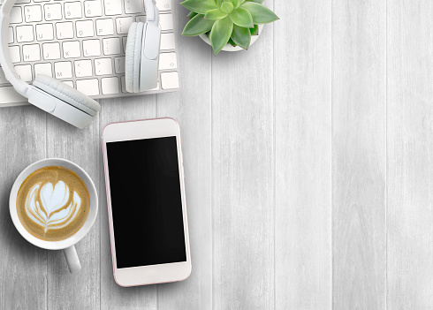 Smartphone black screen, white head phone,keyboard  and cup of coffee on white wood table background, mockup modern smartphone jet black color.Top view with copy space for use.