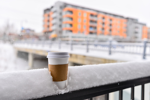 A coffee cup in snow with a winter city backdrop. Photo taken during a snowfall in the winter in Minneapolis, Minnesota.