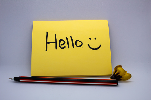 Close-up selected focus isolated Yellow Sticky note with hello greeting and smiley face written on it with some romantic elements on white background