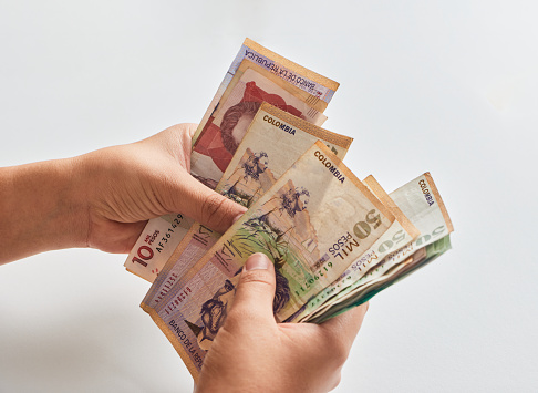 Man's hands holding Colombian banknotes on white background in close-up