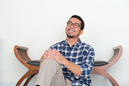 Adult Asian man sitting relax while imagine something with happy expression