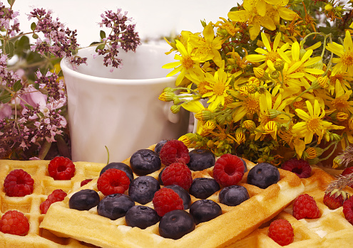 Viennese cookies with raspberries and blueberries. A bouquet of meadow flowers, a cup of tea or coffee. Morning summer breakfast. Side view. Close-up.