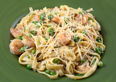 Shrimp pasta dish with peas and bacon and cream sauce on green plate