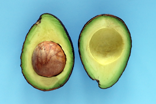 Stock photo showing an avocado cut in half displaying its large seed and rind around edge, healthy eating concept.