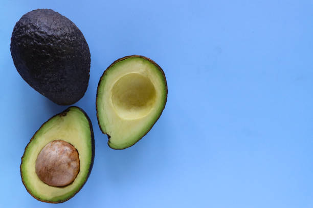 istock Close-up image of one whole and one halved avocado fruit, cross sections displaying large seed, blue background, elevated view, copy space 1410939737