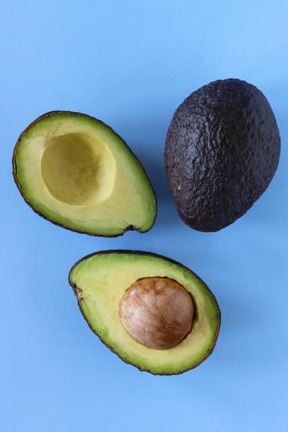istock Close-up image of one whole and one halved avocado fruit, cross sections displaying large seed, blue background, elevated view 1410939739