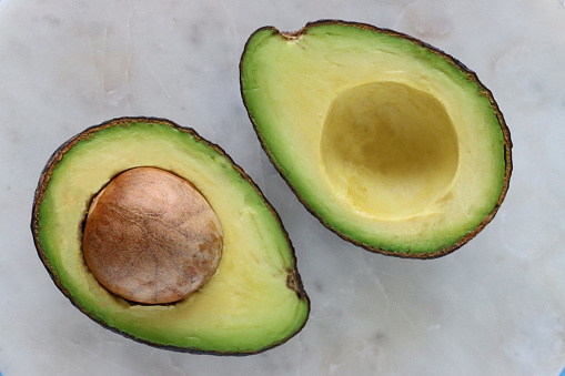 Stock photo showing an avocado cut in half displaying its large seed and rind around edge, healthy eating concept.