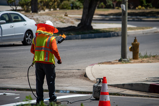 Northridge, California, United States -  June 28, 2022: A contractor from Paveco Construction working for the City of Los Angeles uses a torch to dry a newly painted \