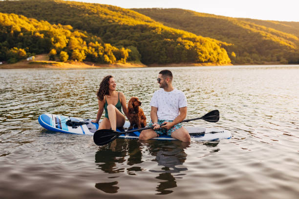 Young loving couple having fun while paddling on a paddle board on the lake