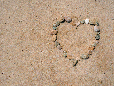 Set of colorful pebbles forming a heart shape on beach sand background