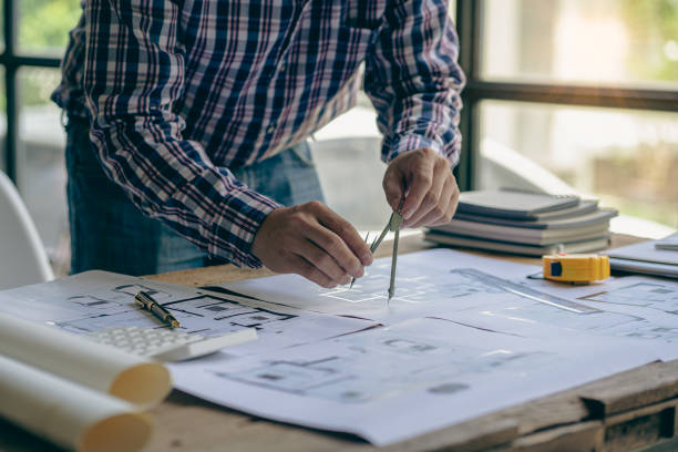 istock Close-up of a man working on a project sketching architects on blueprints at a construction site. Architect, engineer concept in desk construction project bannerclose-up of drawing plans with architect equipment 1410957288