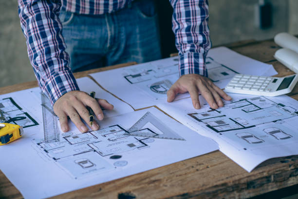 istock Close-up of a man working on a project sketching architects on blueprints at a construction site. Architect, engineer concept in desk construction project bannerclose-up of drawing plans with architect equipment 1410957289