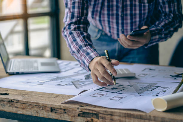 istock Close-up of a man working on a project sketching architects on blueprints at a construction site. Architect, engineer concept in desk construction project bannerclose-up of drawing plans with architect equipment 1410957320