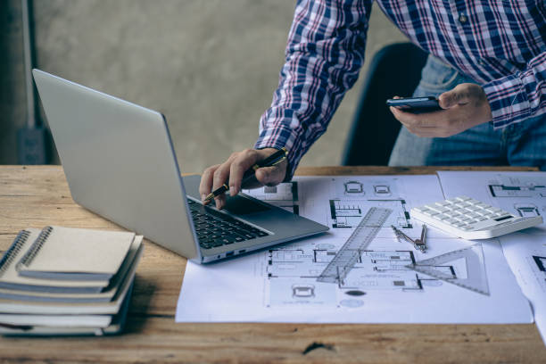 istock Close-up of a man working on a project sketching architects on blueprints at a construction site. Architect, engineer concept in desk construction project bannerclose-up of drawing plans with architect equipment 1410957322