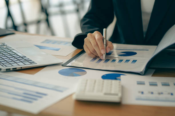 istock Businessman holding pen and paper pointing chart summary analysis calculating annual business report using laptop at desk in office concept accounting 1410957529