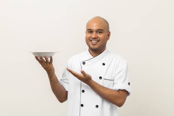 istock Smiling Young handsome asian man chef in uniform holding empty plate delicious dish menu good taste on isolated. Cooking indian man Occupation chef or baker People in kitchen restaurant and hotel. 1410957593